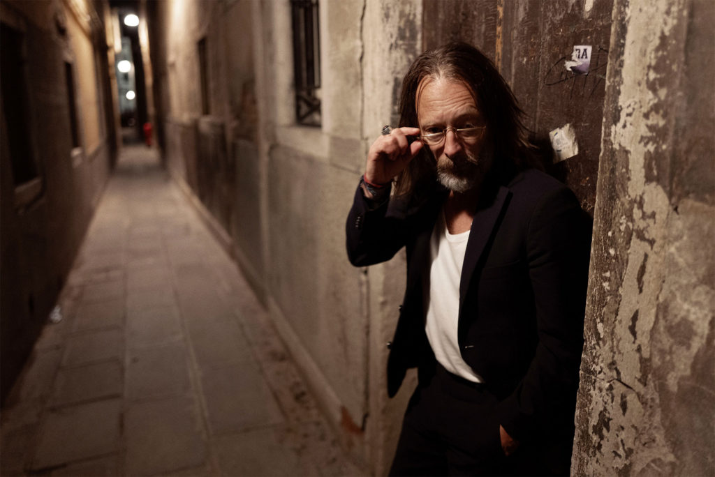 Photo of Thom Yorke in an alley that looks like a medieval town in Southern Europe. Kind of like the scenery of 'Only Lovers Left Alive' by Jim Jarmusch. Probably Taken by Greg Williams